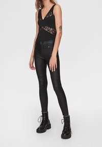 Svart bodysuit med spetsdetaljer, parat med svarta skinny jeans med dragkedjefickor och svart lace-up combat boots.