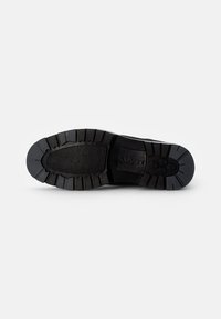 Suela de zapatilla de goma negra con textura acanalada, que presenta un dibujo en relieve y un logotipo de la marca. El diseño enfatiza la tracción y la durabilidad.