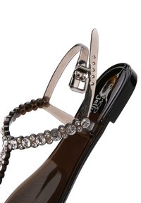Sandalo nero con cinturini trasparenti, decorato con strass circolari. Presenta una punta arrotondata e una fibbia regolabile alla caviglia. Finitura liscia e lucida.
