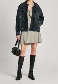 Svart denimjacka, grön klänning med ett strukturerat mönster, knähöga svarta klackstövlar och en liten svart handväska.