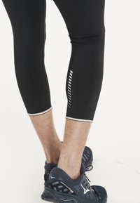Svarta träningsleggings med slim fit, med reflekterande detaljer och ett vitt geometriskt mönster på sidan, tillsammans med mörka löparskor.
