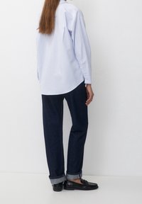 Lichtblauwe en witte gestreepte lange mouwen shirt gecombineerd met donkerblauwe rechte jeans; de schoenen zijn zwarte loafers met een gladde afwerking.