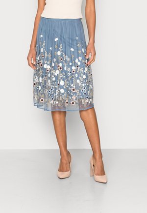 Jasnoniebieska spódnica midi z kwiatowym haftem w kolorach białym, różowym i czarnym. Posiada marszczoną talię i przezroczystą warstwę, zestawiona z beżowymi szpilkami.