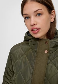 Olijfgroene gewatteerde jas met een capuchon, met een soepele textuur, opvallende stiksels en bronzen accenten.