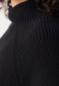 Pull en tricot noir avec un col haut et une texture côtelée. Présente des motifs verticaux et une coupe près du corps.