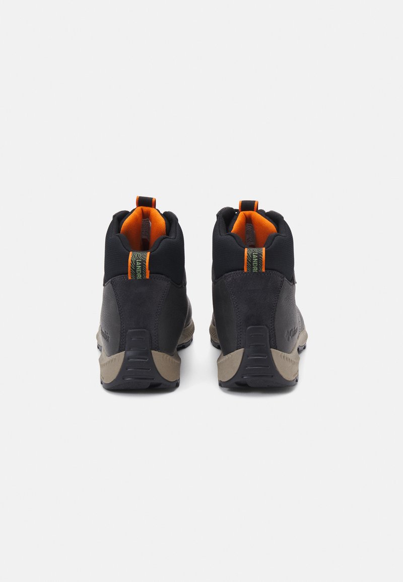 Zapatos de senderismo negros con parte superior de ante y textil, suela de goma y acentos naranjas. Cuenta con un collar acolchado y asas para facilitar su uso.