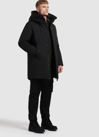 Parka neagră cu guler înalt și glugă mare, având un fermoar frontal, buzunare laterale și o croială lejeră, asortată cu pantaloni cargo negri și bocanci.