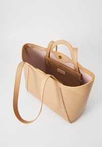 Beige leather tote bag with structured design, dual handles, and an inner zip pocket. Lined in light pink fabric for contrast.