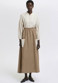 Lang beige nederdel med sidelommer, parret med en lys beige skjorte med krave og knapper. Stofudtrykket ser tekstureret ud med en afslappet pasform.