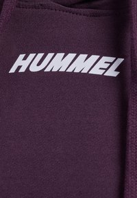 Lila Sweatshirt aus strukturiertem Material, mit einem auffälligen weißen "HUMMEL"-Logo, das quer über die Brust angebracht ist.