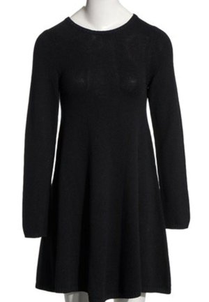 Vestido negro de punto con mangas largas, escote redondo y falda acampanada, mostrado en un maniquí.