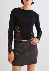 Maglietta nera a maniche lunghe con dettagli in pizzo sulle maniche, abbinata a una gonna grigia a righe sottili. Presenta un design aderente e una texture liscia.