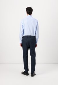 Light blue long-sleeve shirt with button cuffs, paired with dark navy stretch trousers featuring an elastic waistband and pockets. Black shoes visible.