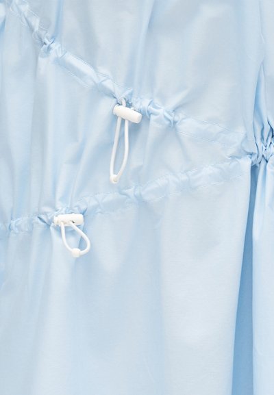 Ανοιχτό μπλε ύφασμα με δύο λευκά ρυθμιζόμενα κορδόνια με πλαστικά κλιπ που δημιουργούν σφιχτές πιέτες.
