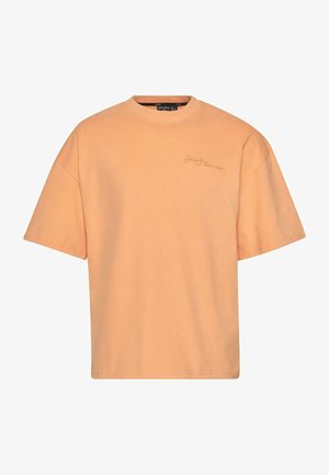 T-shirt à manches courtes en coton doux pêche. Encolure ronde, coupe ample, avec un logo brodé subtile sur le devant pour plus de détails.