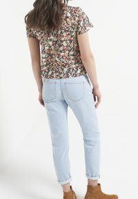 Haut à manches courtes à motifs floraux multicolores, assorti à un jean bleu clair avec revers et des bottines marron clair.