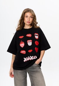 Zwarte oversized t-shirt met kleurrijke grafische ontwerpen van lippen en gezichten in rood en roze. De tekst "xoxo" staat in vetgedrukte witte letters.
