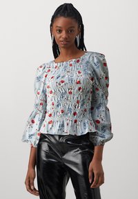 Blusa a righe blu con motivi floreali, corpino arricciato e maniche a sbuffo. Abbinata a pantaloni aderenti neri lucidi.