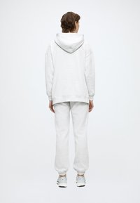 Ανοιχτό γκρι φούτερ με άνετη εφαρμογή, ριμπ μανσέτες και μεγάλη κουκούλα, συνδυασμένο με αντίστοιχο παντελόνι φόρμας με μανσέτες. Μαλακό βαμβακερό ύφασμα.