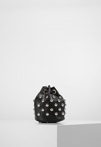 Borsa a secchiello nera decorata con borchie argentate, posizionata su una superficie grigia chiara contro uno sfondo bianco uniforme.