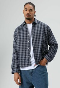 Herren-Flanellhemd im Marine- und Grau-Karomuster mit durchgehender Knopfleiste, langen Ärmeln und entspannter Passform, getragen über einem weißen T-Shirt.