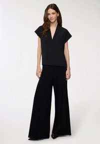 Top nero a maniche corte con scollatura a V, abbinato a pantaloni neri a gamba larga. Tessuto liscio con una silhouette elegante e moderna.