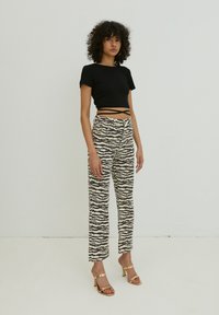 Schwarzes Cropped-Top mit kurzen Ärmeln, kombiniert mit hochgeschnittenen Hosen, die ein Zebra-Streifenmuster in Beige und Dunkelbraun aufweisen. Goldene Absatzsandalen.