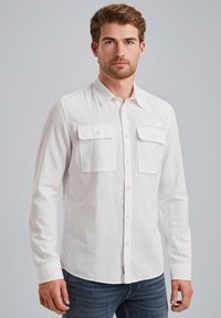 Camisa blanca de manga larga hecha de tejido ligero, con un frente abotonado, cuello puntiagudo y dos bolsillos en el pecho con solapas.