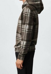 Sudadera con capucha de cuadros marrones, hecha de forro polar, con capucha, mangas largas y un ajuste relajado. El patrón incluye tonos más claros y oscuros de marrón.