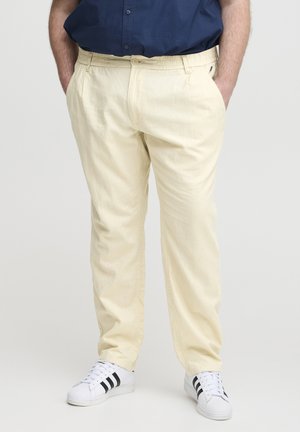 Light yellow linen pants with a relaxed fit, featuring an elastic waistband, front pockets, and slightly tapered legs. Paired with white sneakers.
