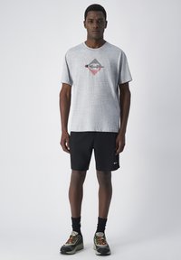 Camiseta gris de manga corta con gráfico en negro y rojo, combinada con pantalones cortos negros y zapatillas deportivas multicolores. Diseño simple y casual.