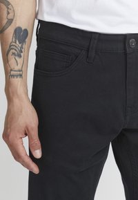 Crne pamučne hlače slim kroja, s prednjim džepom, petljama za remen i metalnim dugmetom za zatvaranje. Glatka tekstura s minimalnim detaljima.