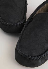 Sorte ruskind mokkasinslippers med rund tå, der har en flettet kant og blød tekstur. Indersiden har et vævet mønster for ekstra detalje.