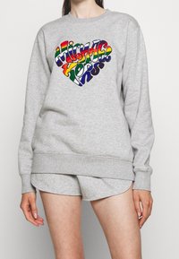 Felpa grigia con polsini e orlo a coste, caratterizzata da un logo a forma di cuore multicolore con il testo "Michael Kors" in vivaci colori dell'arcobaleno.