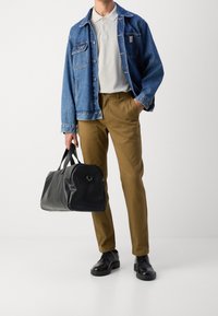 Zwarte leren sporttas met afgeronde hoeken, gecombineerd met een denim jack, licht polo shirt en kaki broek. Zwarte schoenen maken de outfit compleet.