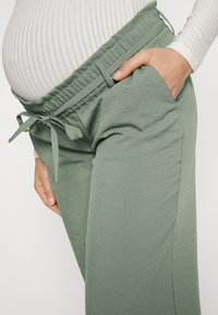 Graviditetsbyxor i ljusgrön tyg, med elastisk midja och dragsko, sidofickor och mjuk, slät yta.