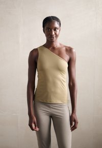 Top a spalla asimmetrico in tessuto beige, texture liscia, design aderente, abbinato a leggings beige chiari.