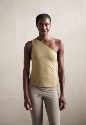 Asymmetrical one-shoulder tank top in tan fabric, smooth texture, fitted design, paired with light beige leggings.