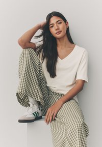 T-shirt cremosa con scollo a V, pantaloni a gamba larga a quadretti verdi e bianchi, e sneaker bianche con dettagli verdi. Tessuti lisci, vestibilità comoda.