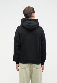 Must värvi kapuutsiga sviitri lõtva lõikega, ribaga mansetid ja lühendatud serv, koos heledate denimiste teksadega.