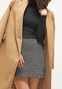 Černý žebrovaný rolák, béžový vlněný kabát s velkými klopami a šedá miniskirt v houndstooth vzoru. Hladké textury a kontrastní barvy.
