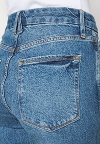 Jeans de mezclilla azules de cintura alta con un diseño clásico de cinco bolsillos, textura desgastada y costuras en contraste a lo largo de las costuras.