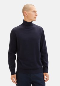 Granatowy sweter z golfem wykonany z miękkiego materiału dzianinowego. Posiada długie rękawy oraz dopasowany krój z prążkowanym kołnierzem i dołem.