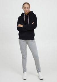 Black, fluffy hoodie with a drawstring hood, white accents, and a logo. Paired with light gray slim-fit pants and white sneakers.