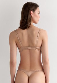 Ensemble de lingerie nude avec bretelles réglables, délicats accents en dentelle et finition lisse. Fermeture à agrafes au dos pour un ajustement sécurisé.