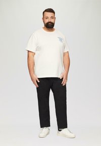 T-shirt en coton crème à manches courtes avec texte bleu, pantalon en coton noir et baskets blanches avec accents noirs. Pas de motifs, design simple.