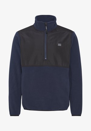 Navy fleece pullover with a black nylon chest panel, quarter zip, stand collar, and side pockets. Features a logo patch on the chest.