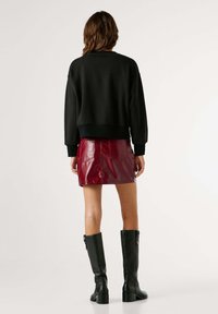 Melns saīsināts sporta krekls ar garām piedurknēm, komplektā ar sarkanu lakādas mini svārku. Modelis valkā augstus melnus zābakus ar masīvu papēdi.