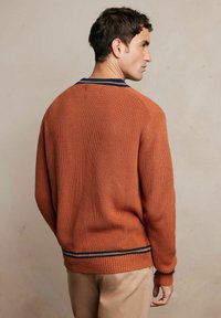 Sweter w kolorze rdzawym, prążkowany, z okrągłym dekoltem, z granatowym i kremowym paskiem na kołnierzyku i dolnym brzegu.