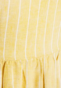 Žlutá látka s bílými svislými pruhy, se staženým lemem a textura povrchu. Design je lehký a měkký.